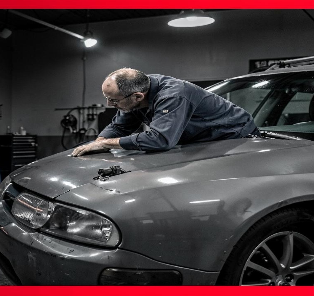 Automotive technician examining the hood of a vehicle in a workshop